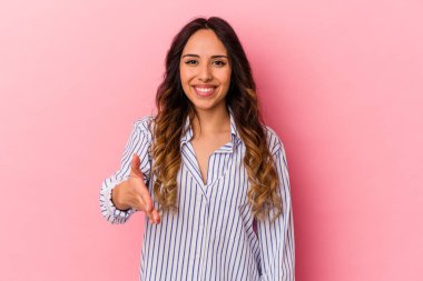 Pembe arka planda izole edilmiş genç Meksikalı kadın selamlaşma jesti olarak kameraya uzanıyor..