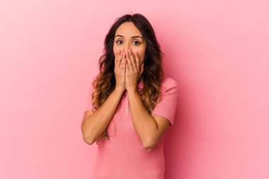 Pembe arka planda izole edilmiş genç Meksikalı kadın şok olmuş, elleri ağızda, yeni bir şey keşfetmek için sabırsızlanıyor..