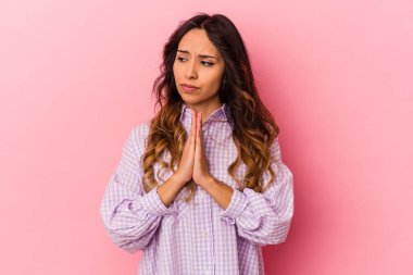 Genç Meksikalı kadın pembe arka planda izole edilmiş dua ediyor, bağlılık gösteriyor, dindar biri ilahi ilham arıyor..