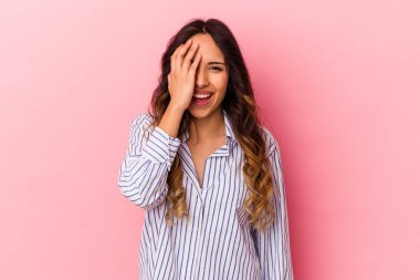 Pembe arka planda izole edilmiş genç Meksikalı kadın yüzünün yarısını avuç içiyle örterek eğleniyor..