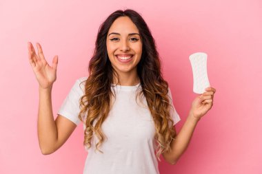 Pembe arka planda bir kompres tutan genç Meksikalı kadın hoş bir sürprizle karşılaşıyor, heyecanlı ve el kaldırıyor..