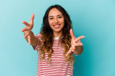 Mavi arka planda izole edilmiş genç Meksikalı kadın kameraya sarıldığı için kendinden emin..