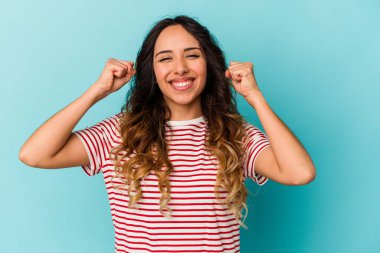 Mavi arka planda izole edilmiş genç Meksikalı kadın zaferi, tutkuyu ve coşkuyu kutluyor, mutlu bir ifade..