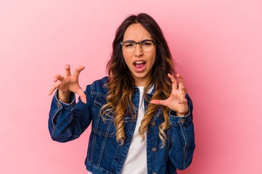 Pembe arka planda izole edilmiş genç Meksikalı kadın pençelerini kedi taklidi yaparken gösteriyor, agresif bir hareket..