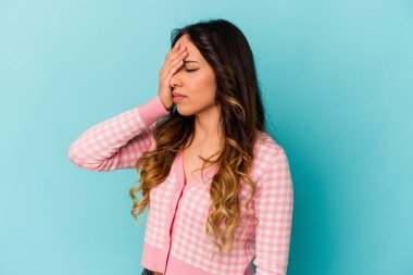 Mavi arka planda izole edilmiş genç Meksikalı kadın başı ağrıyor, yüzüne dokunuyor..