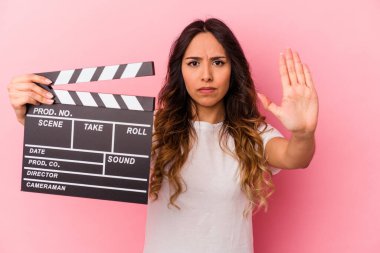 Pembe arka planda elinde klaket tutan genç Meksikalı kadın elini uzatıp dur işareti göstererek seni engelliyor..