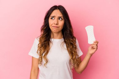 Pembe arka planda bir kompres tutan genç Meksikalı kadın şaşkın ve kararsız hissediyor..