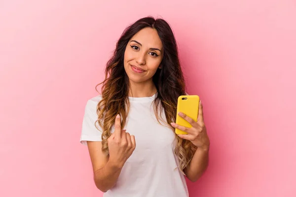 年轻的墨西哥女人拿着一部粉色背景的手机 用手指指着你 好像邀请你走近些 — 图库照片