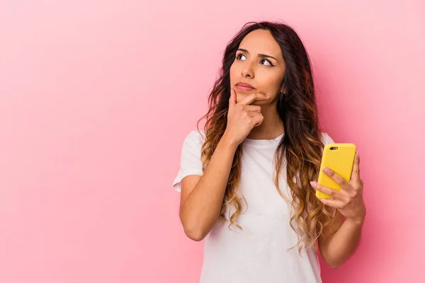 Joven Mexicana Sosteniendo Teléfono Móvil Aislado Sobre Fondo Rosa Mirando —  Fotos de Stock