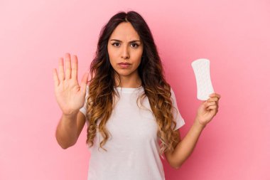 Genç Meksikalı bir kadın pembe arka planda izole edilmiş bir kompres tutuyor elini uzatmış, dur işareti veriyor ve seni engelliyor..