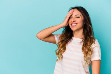 Genç Meksikalı bir kadın mavi arka planda izole edilmiş gülerek, kaygısız, doğal duygularla gülüyor..