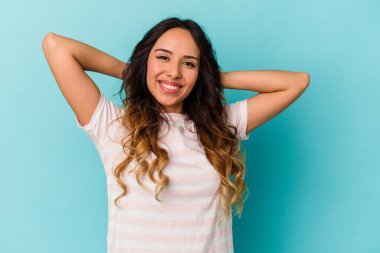 Genç Meksikalı kadın mavi arka planda izole edilmiş. Kendine güveniyor, elleri başının arkasında..