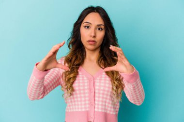 Mavi arka planda izole edilmiş genç Meksikalı kadın elinde avuç içi bir şeyle kameraya sunuyor..