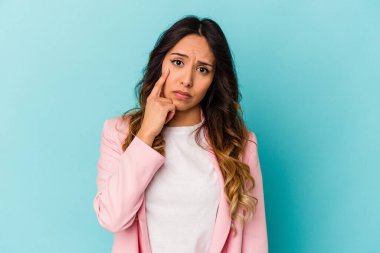 Genç Meksikalı kadın mavi arka planda izole edilmiş, ağlıyor, bir şeyden memnun değil, acı ve kafa karışıklığı konsepti..