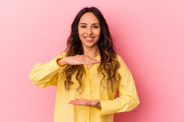 Pembe arka planda izole edilmiş genç Meksikalı kadın iki eliyle bir şey tutuyor, ürün sunumu..