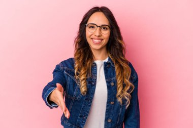 Pembe arka planda izole edilmiş genç Meksikalı kadın selamlaşma jesti olarak kameraya uzanıyor..