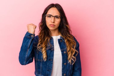 Pembe arka planda izole edilmiş genç Meksikalı kadın yumruğunu kameraya gösteriyor, agresif yüz ifadesi..
