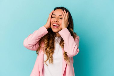 Mavi arka planda izole edilmiş genç Meksikalı kadın mutlu bir şekilde ellerini başının üstünde tutuyor. Mutluluk kavramı.