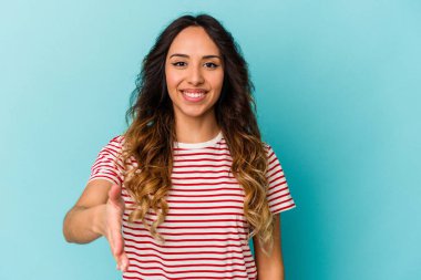 Mavi arka planda izole edilmiş genç Meksikalı kadın selamlama jesti olarak kameraya elini uzatıyor..