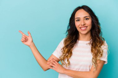 Mavi arka planda izole edilmiş genç Meksikalı kadın işaret parmağıyla işaret ederek gülümsüyor..