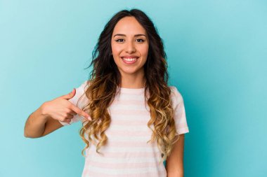 Mavi arka planda izole edilmiş genç Meksikalı kadın gömlek fotokopi alanını elle işaret ediyor, gururlu ve kendinden emin.