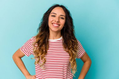 Mavi arka planda izole edilmiş genç Meksikalı kadın ellerini kalçasından ayırmıyor..