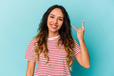 Mavi arka planda izole edilmiş genç Meksikalı kadın parmaklarıyla kaya hareketi gösteriyor.