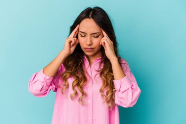 Mavi arka planda izole edilmiş genç Meksikalı kadın tapınaklara dokunuyor ve baş ağrısı çekiyor..