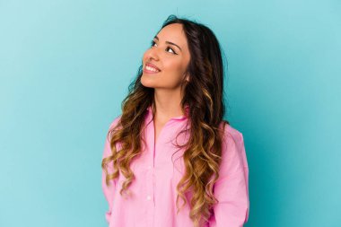 Mavi arka planda izole edilmiş genç Meksikalı kadın rahat ve mutlu bir şekilde gülüyor, boynunda dişlerini gösteriyor..