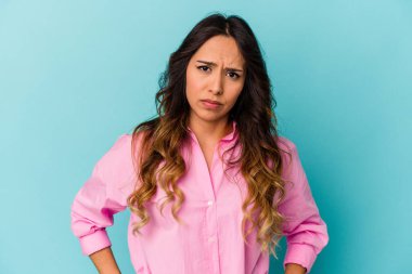 Mavi arka planda izole edilmiş genç Meksikalı kadın kafası karışmış, şüpheli ve güvensiz hissediyor..