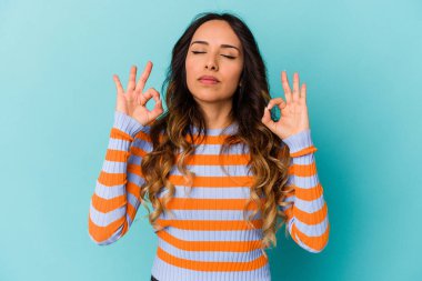 Mavi arka planda izole edilmiş genç Meksikalı kadın yoğun bir günün ardından rahatlıyor, yoga yapıyor..