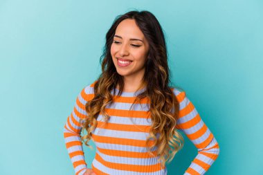 Mavi arka planda izole edilmiş genç Meksikalı kadın ellerini kalçasından ayırmıyor..