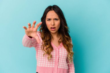 Mavi arka planda izole edilmiş genç Meksikalı kadın pençelerini kedi taklidi yaparken gösteriyor, agresif bir hareket..