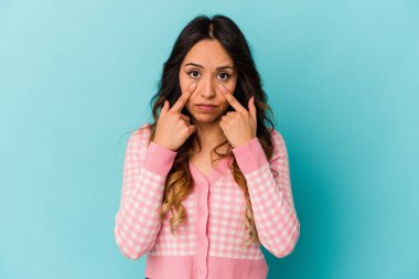 Genç Meksikalı kadın mavi arka planda izole edilmiş, ağlıyor, bir şeyden memnun değil, acı ve kafa karışıklığı konsepti..