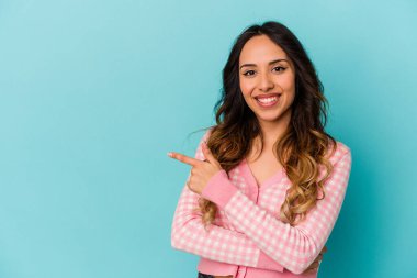 Mavi arka planda izole edilmiş genç Meksikalı kadın işaret parmağıyla işaret ederek gülümsüyor..