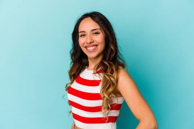 Mavi arka planda izole edilmiş genç Meksikalı kadın ellerini kalçasından ayırmıyor..