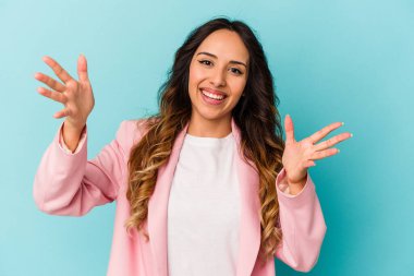 Mavi arka planda izole edilmiş genç Meksikalı kadın zaferi veya başarıyı kutluyor, şaşırıyor ve şok oluyor..