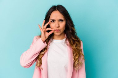 Mavi arka planda izole edilmiş genç Meksikalı kadın parmakları dudaklarında bir sır saklıyor..