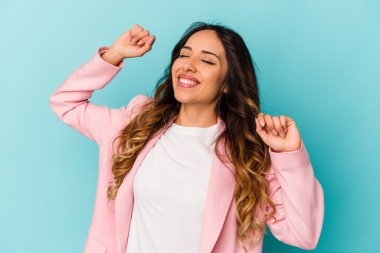 Mavi arka planda izole edilmiş genç Meksikalı kadın özel bir günü kutluyor, atlıyor ve enerjiyle kollarını kaldırıyor..