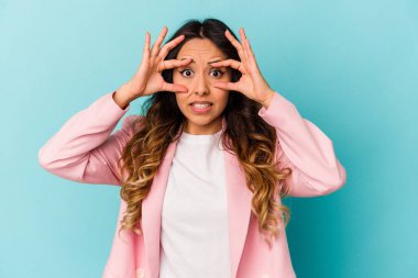 Mavi arka planda izole edilmiş genç Meksikalı kadın bir başarı fırsatı bulmak için gözlerini açık tutuyor..