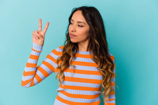 Mavi arka planda izole edilmiş genç Meksikalı kadın neşeli ve tasasız parmakları olan bir barış sembolü gösteriyor..