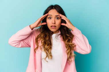 Mavi arka planda izole edilmiş genç Meksikalı kadın hoş bir sürprizle karşılaşıyor, heyecanlı ve el kaldırıyor..