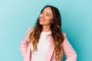 Mavi arka planda izole edilmiş genç Meksikalı kadın rahat ve mutlu bir şekilde gülüyor, boynunda dişlerini gösteriyor..