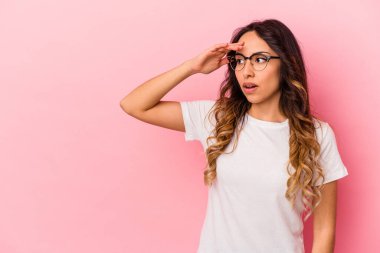 Pembe arka planda izole edilmiş genç Meksikalı kadın uzaklara bakıyor ve elini alnına koyuyor..