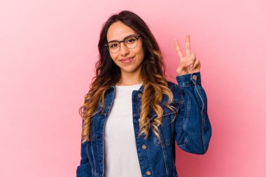 Pembe arka planda izole edilmiş genç Meksikalı kadın neşeli ve tasasız parmakları olan bir barış sembolü gösteriyor..