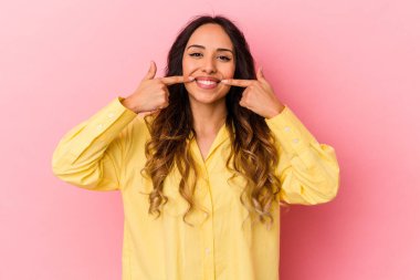 Pembe arka planda izole edilmiş genç Meksikalı kadın gülümsüyor, parmaklarını ağıza doğrultuyor..