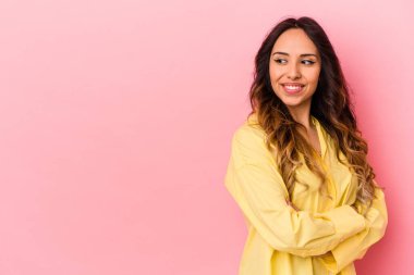 Pembe arka planda izole edilmiş genç Meksikalı kadın kollarını kavuşturarak gülümsüyor..