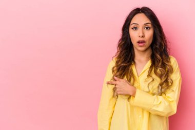 Pembe arka planda izole edilmiş genç Meksikalı kadın gülümsüyor ve boş alanda bir şeyler gösteriyor..