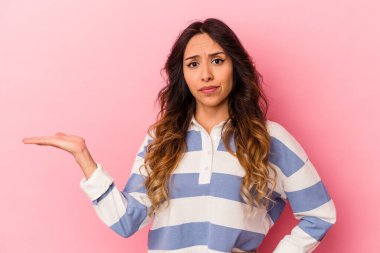 Pembe arka planda izole edilmiş genç Meksikalı kadın sorgulama sırasında omuz silkiyor ve şüphe duyuyor..