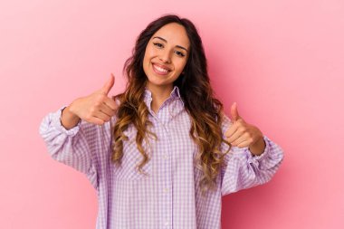Pembe arka planda izole edilmiş genç Meksikalı kadın iki parmağını da kaldırıyor, gülümsüyor ve kendinden emin..